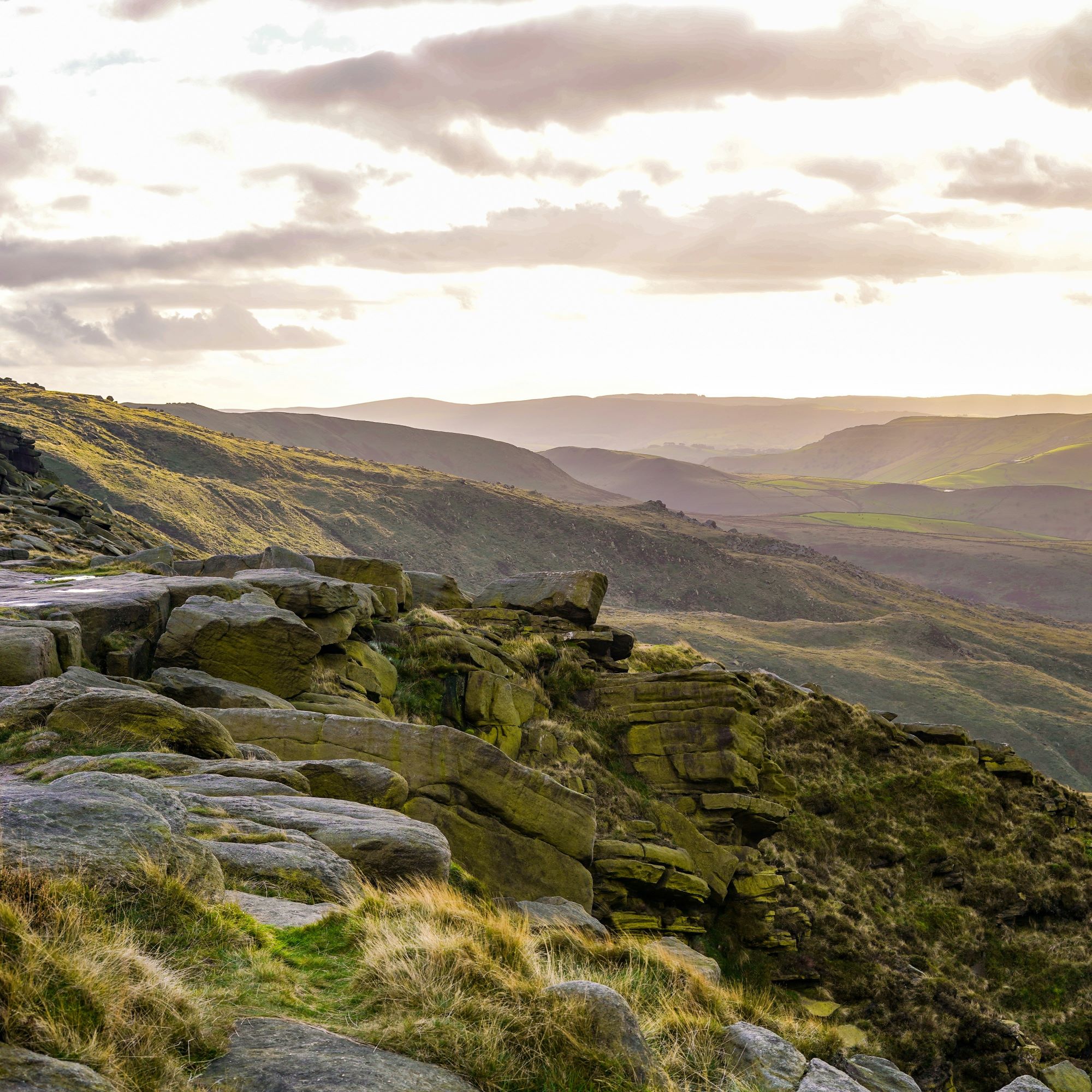 a rocky cliff in the peak district surrounded by fields