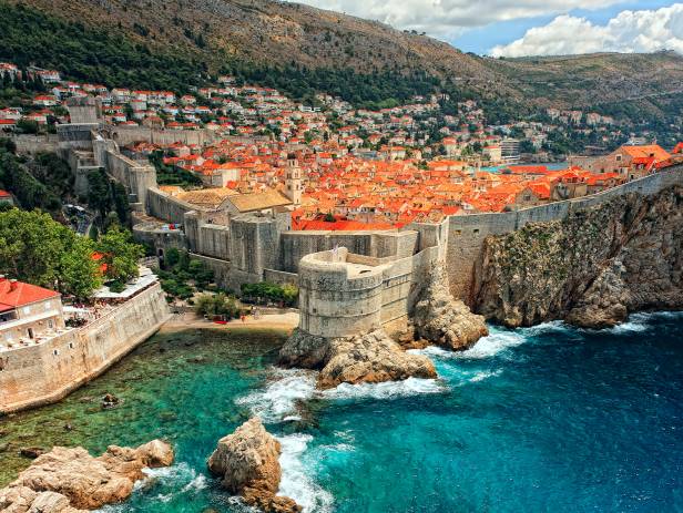 Aerial view of Dubrovnik, surrounded by water and filled with terracotta-roofed buildings